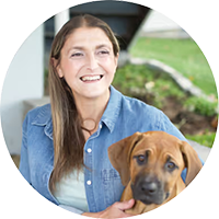 Smiling SBS Connect mentor seated outside, holding a brown dog and ready to share her experience